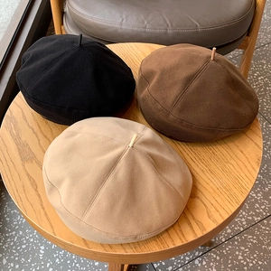 Classic wool beret hats in black, brown, and beige colors on a wooden table