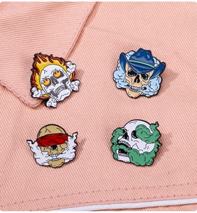 Detail of four punk skeleton enamel pins with flame and smoke effects on pink fabric