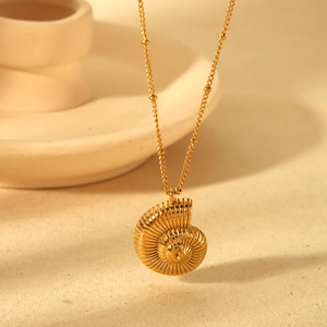 Golden nautilus shell pendant necklace with beaded chain on minimalist tray
