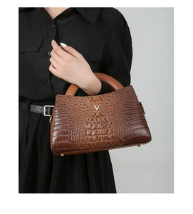 Brown crocodile pattern tote bag with gold V logo held by a model in black dress