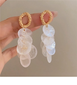 Detail of gold textured round stud earring with cascading white shell pendant tassels