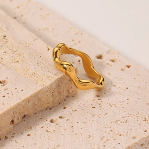 Polished gold wavy geometric titanium steel ring for women on a beige stone background