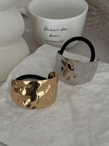 Detail view of gold and silver hammered metal ponytail holders on white artistic backdrop