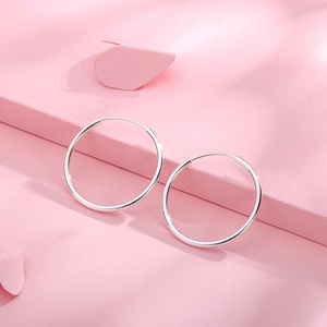Minimalist S999 sterling silver hoop earrings with a polished finish on a pink background