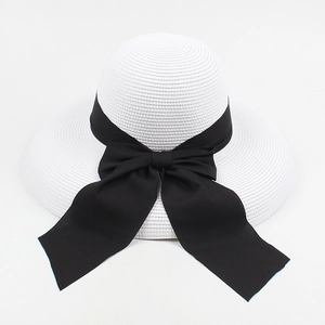 Detailed view of white woven straw hat featuring a large black satin ribbon bow