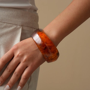 Detail of amber resin chunky bangle with tortoise texture on model in beige outfit