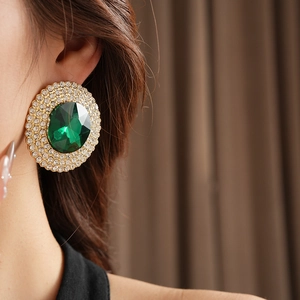 Close-up of emerald green earrings with shimmering diamonds on an elegant model