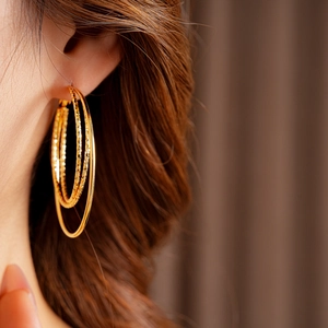 Primer plano de pendientes de aro triples bañados en oro con acabado liso y grabado
