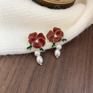 Detailed macro shot of vintage red flower earrings with white pearl pendants on fabric