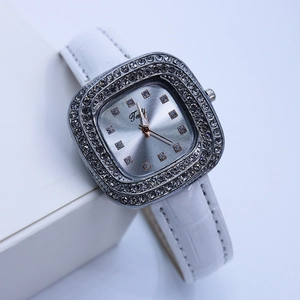 Gros plan d'une montre à quartz carrée avec lunette en diamants et bracelet en cuir blanc