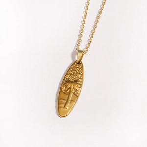 Macro detail of golden surfboard pendant with engraved palm tree on a thin O-chain