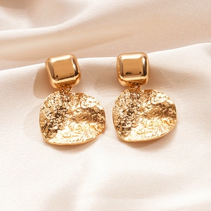 Détail de boucles d'oreilles géométriques dorées avec texture martelée sur de la soie beige