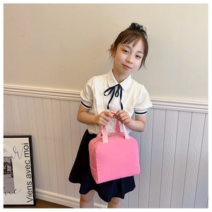 Pink canvas insulated lunch bag for children held by a girl in a cozy indoor setting