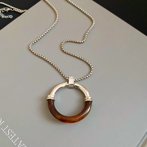 Dettaglio del ciondolo rotondo in metallo argento e resina ambra su collana a catena
