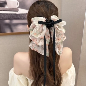 Detailed macro view of an oversized floral bow claw clip with long black ribbons