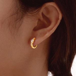 Close-up of gold-plated hoop earring with white zircon inlay worn on an ear