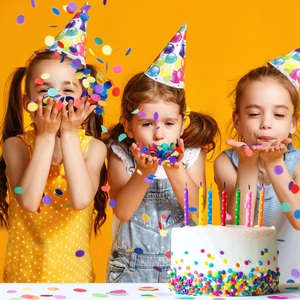 Close-up of colorful candles on a birthday cake with flying confetti and party hats