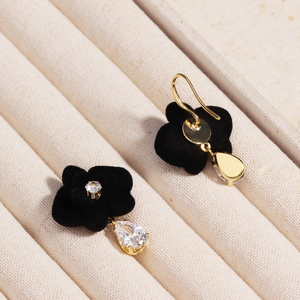 Close-up of geometric black floral earrings with golden tassels and pear-cut zircons