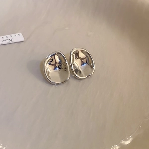 Detail view of silver irregular metallic bean-shaped stud earrings in a textured tray