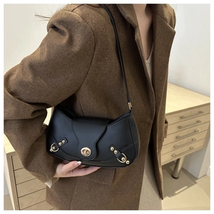 Detail view of black leather underarm bag with gold metal buckle and studs on model
