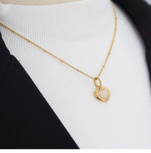 Elegant gold bead chain necklace with a heart shell pendant worn over a chic blazer