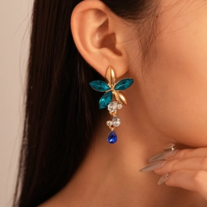 Close-up of model wearing floral crystal drop earring with blue stones and gold finish