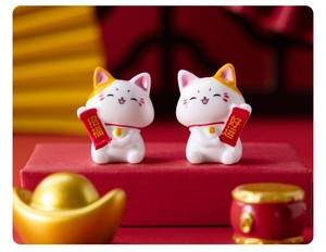 Macro shot of two resin fortune cats holding red scrolls for good luck and blessing