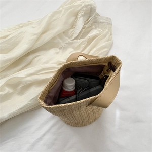 Straw bucket bag with purple lining and daily items on white fabric background