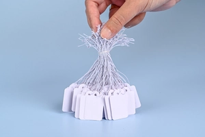 Handheld bundle of blank white paper price tags with strings for jewelry labeling