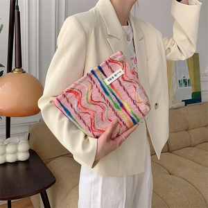 Pink canvas makeup bag with rainbow embroidery held by a model in a cozy living room setting