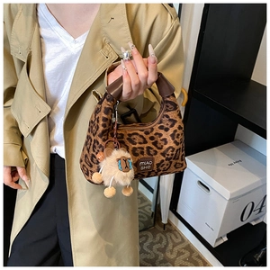 Detailed view of leopard print handbag featuring a plush alpaca charm and brown handle