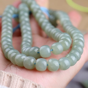 Close-up of pale green Hetian jade beads on a blue string held by a hand