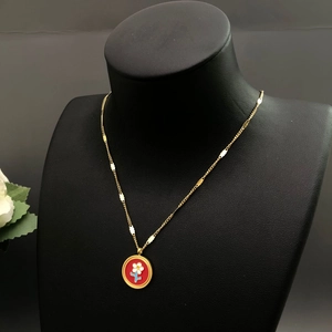 Détail du collier chaîne dorée avec pendentif fleur en émail rouge sur buste