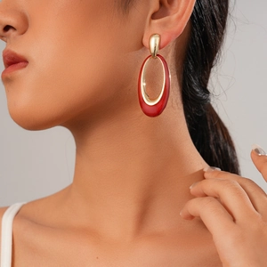 Red enamel oval stud earrings in golden metal frame worn by a model in profile