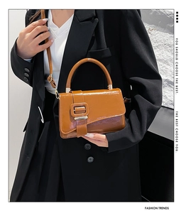 Close-up of caramel glossy leather handbag featuring decorative belt and square buckle detail
