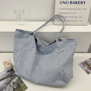 Detail of grey blue tote bag with shiny silver star patterns on white display stand