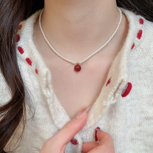 Close-up of 3mm pearl necklace featuring a deep red agate pendant on a white sweater