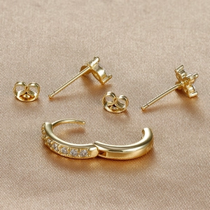 Detail of gold petal earrings and zircon studs on champagne silk fabric background