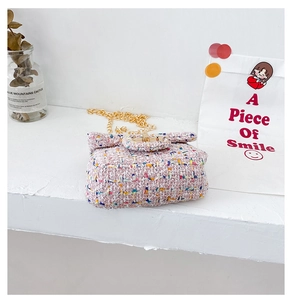 Close-up of pink tweed mini crossbody bag with golden chain strap on a white surface