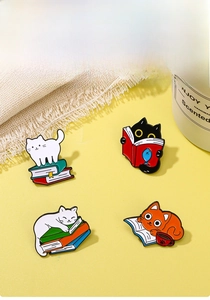 Close-up of four colorful enamel cat pins on books with polished metal finish