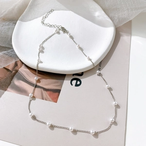 Close-up of minimalist pearl choker with silver chain on white ceramic plate