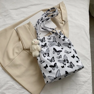 Detail of white canvas tote bag with black butterfly print and plush bear charm decoration
