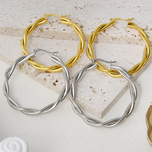 Detailed view of large gold and silver twisted rope hoop earrings on a stone surface