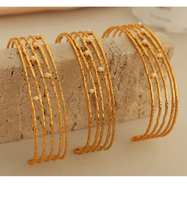 Macro shot of 18K gold C-shaped open bracelets with hammered texture and small pearls