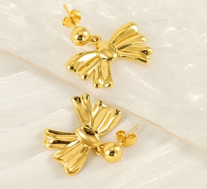 Macro shot of polished gold bow earrings with spherical pendants on silk background