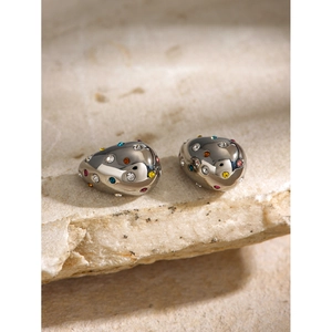 Macro shot of silver teardrop stud earrings with colorful zircons on a rock surface