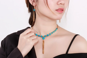 Dettaglio di set collana e orecchini in turchese con nappe dorate sulla modella