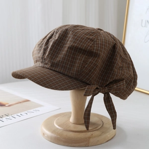 Detail of a brown plaid beret hat featuring a decorative side bow and classic textured fabric