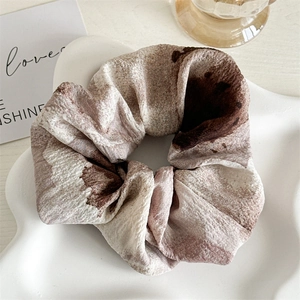 Vue détaillée d'un chouchou en tissu tie-dye beige posé sur un plateau en céramique