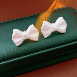 Close-up of pink pearlescent acrylic bow earrings on a premium green leather box